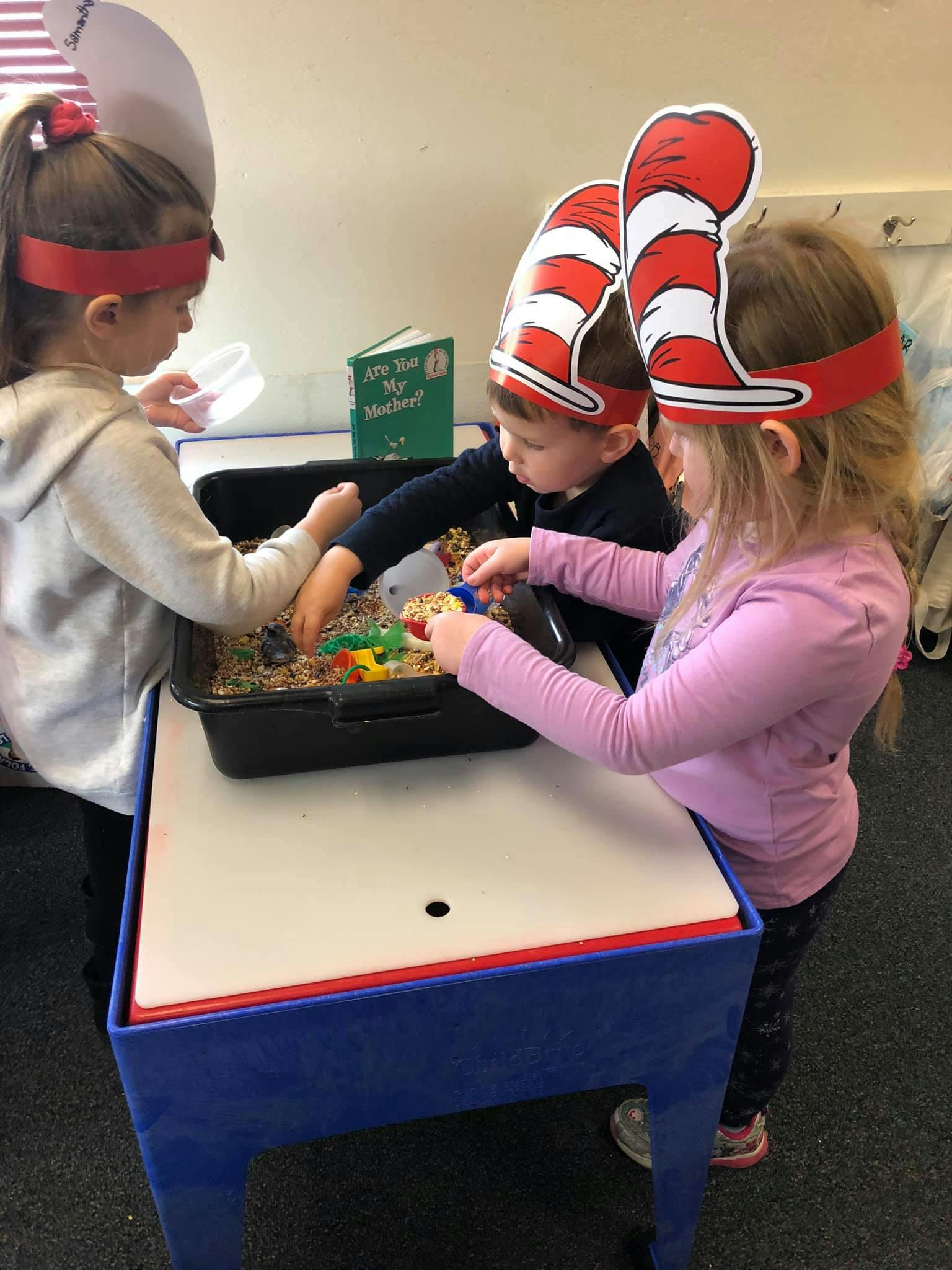 Three children playing with sensory bin materials at a table