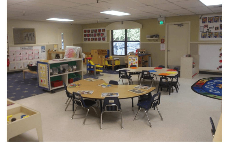 Empty classroom with small tables and chairs, toys, and educational posters