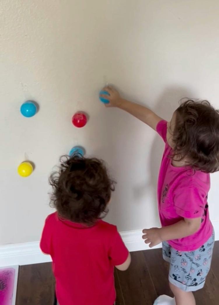 Two children reaching for small colored balls attached to a wall