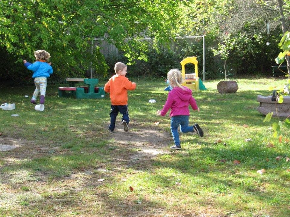 Three children running in a grassy yard