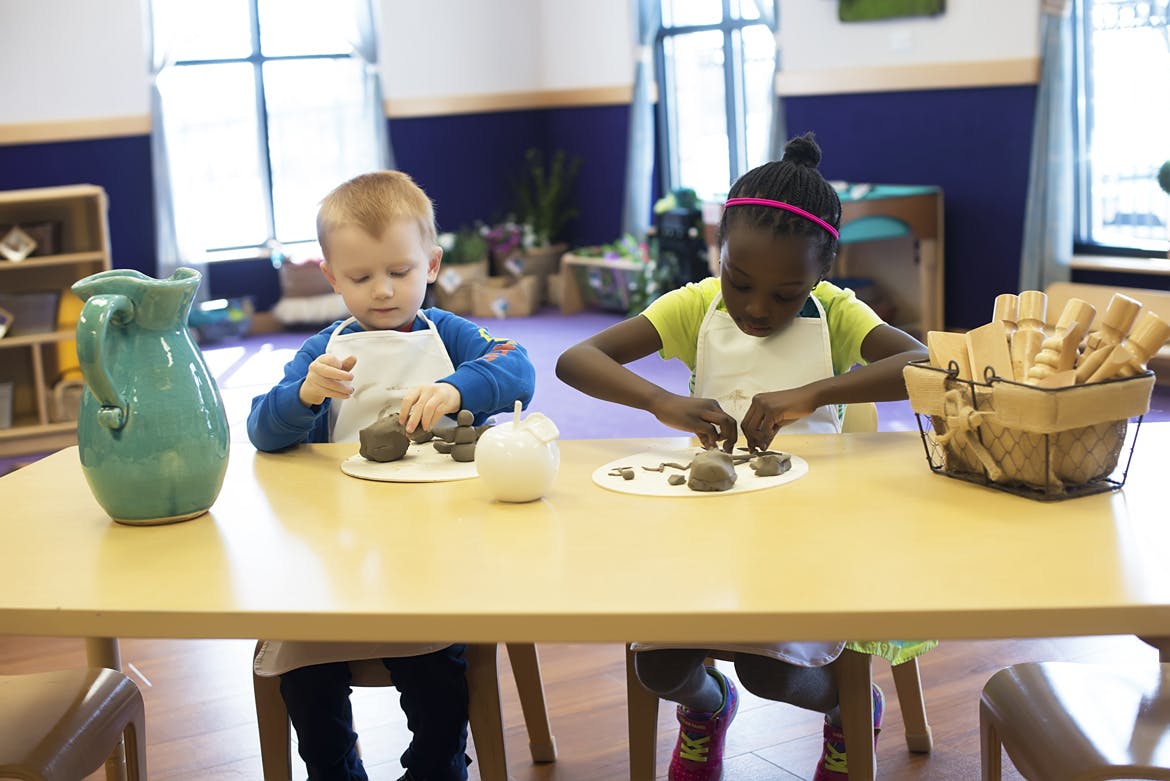 Two children wearing aprons, working with clay at a table