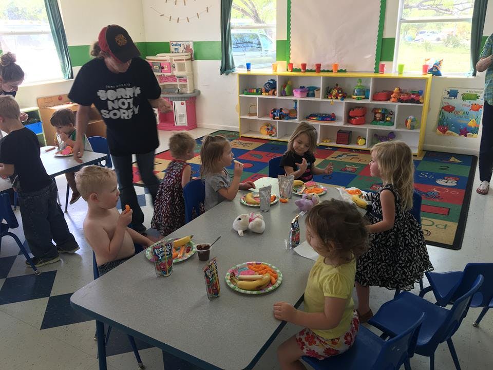 Adult supervising children eating at tables in a classroom