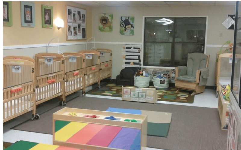 multiple wooden cribs lined up against a wall in a room with a rocking chair