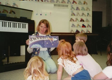 Person kneeling and holding a book with children gathered children