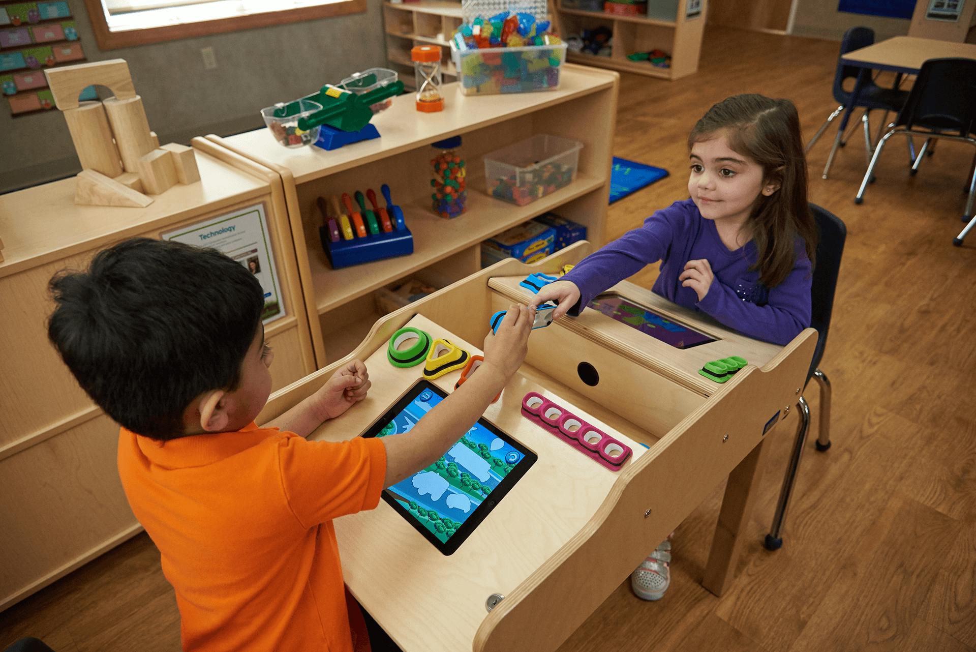 Two children playing with tablets and toys at a table