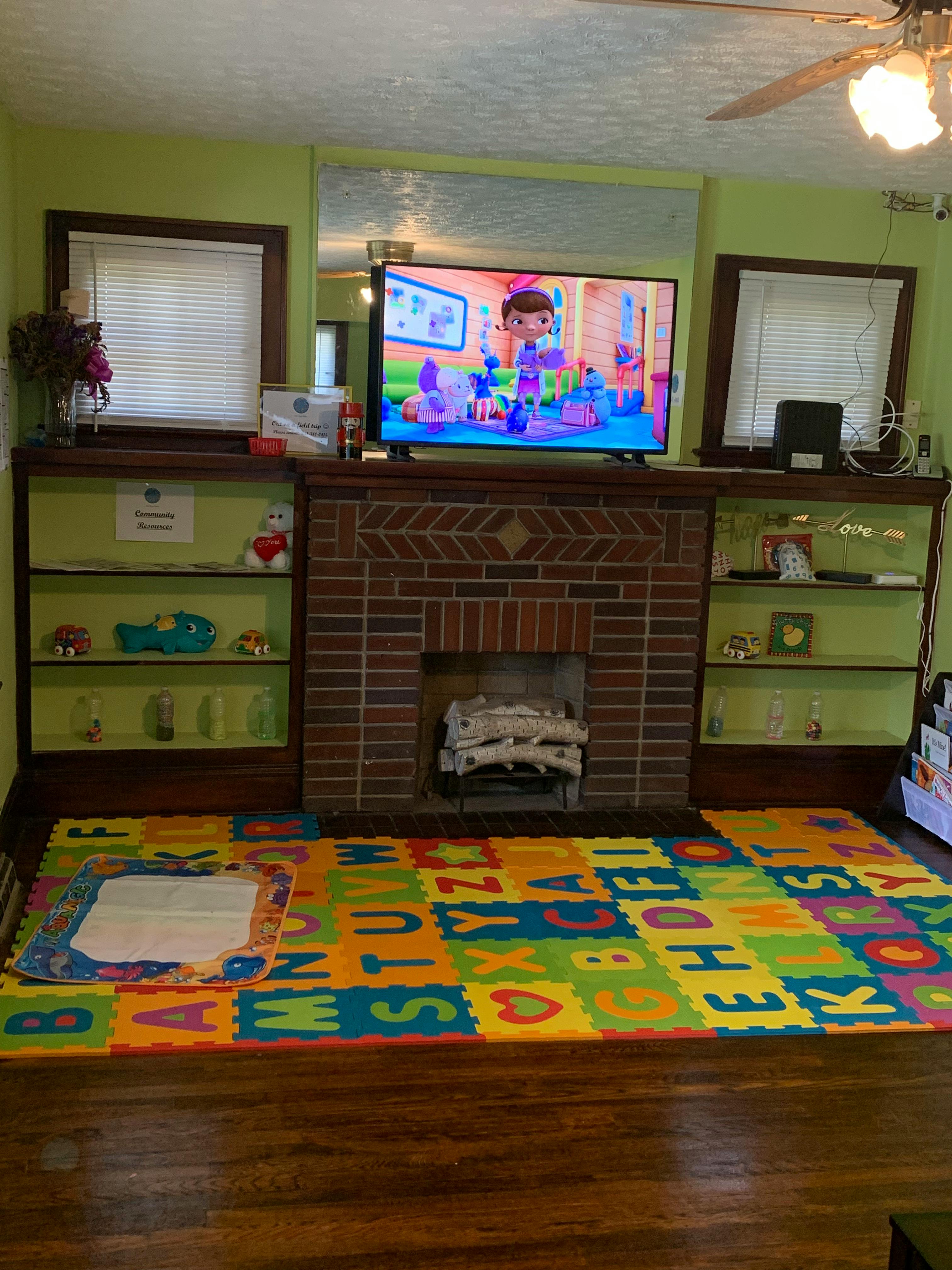 Living room with a TV over a fireplace and an alphabet playmat on the floor