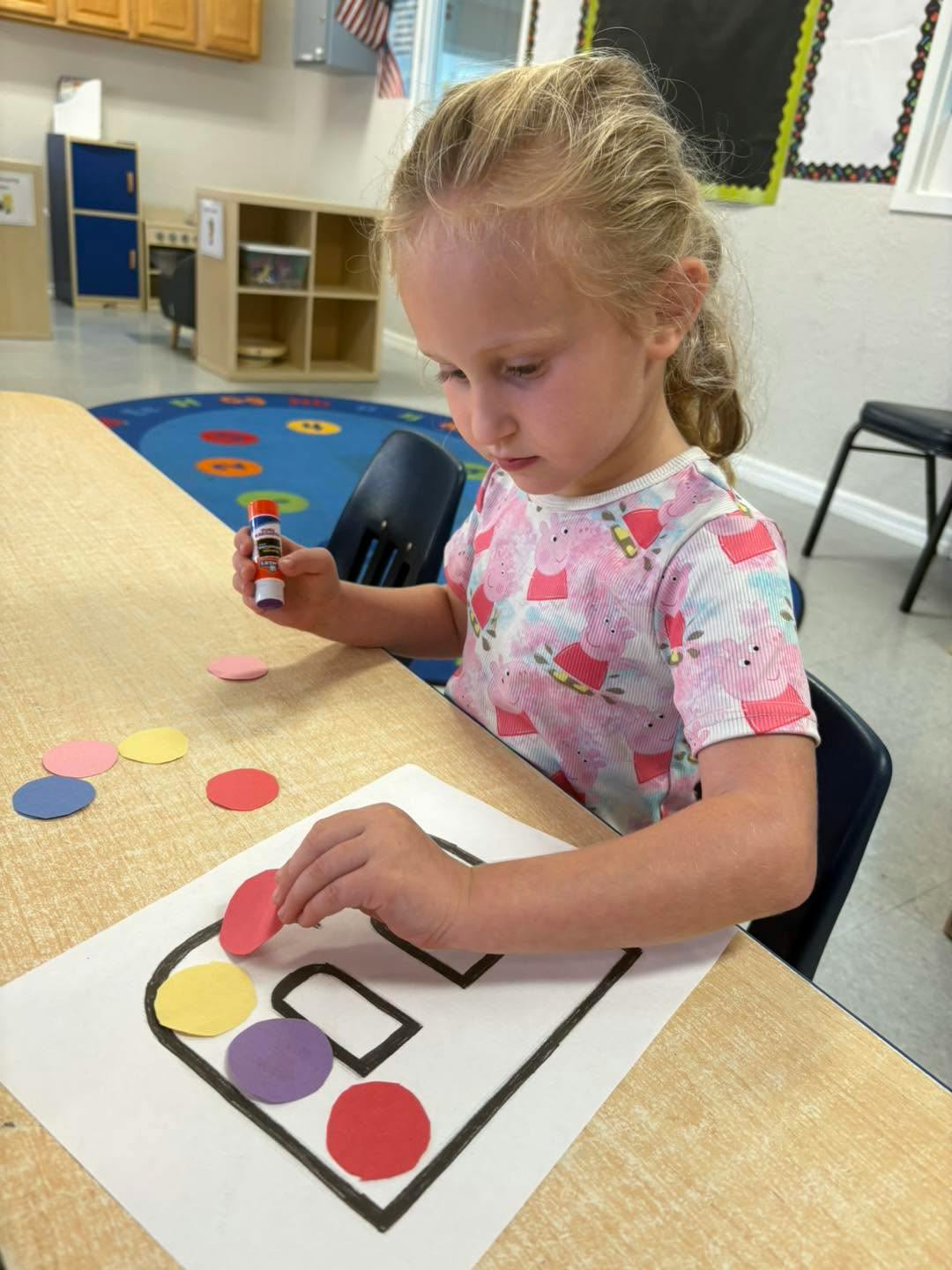 Child gluing paper circles onto a worksheet at a classroom table