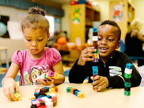 Two children playing with colorful interlocking blocks at a table