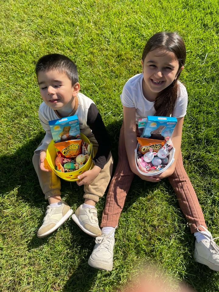 Two children sitting on grass holding baskets filled with items