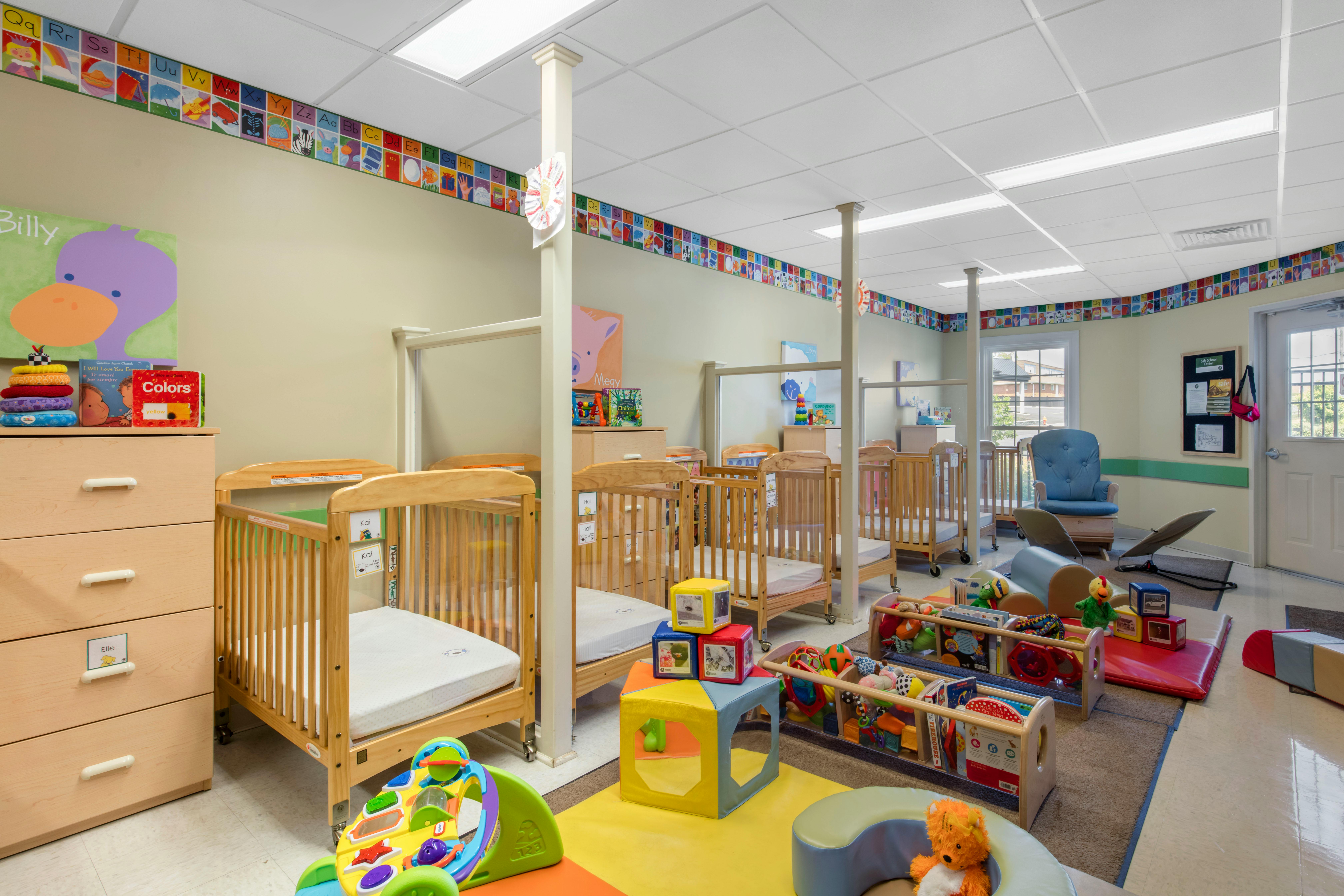 cribs in a daycare room with colorful toys and alphabet trim