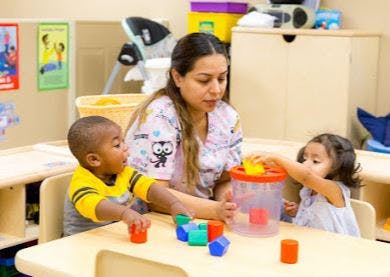 Adult and two children playing with blocks and a shape sorter at a table