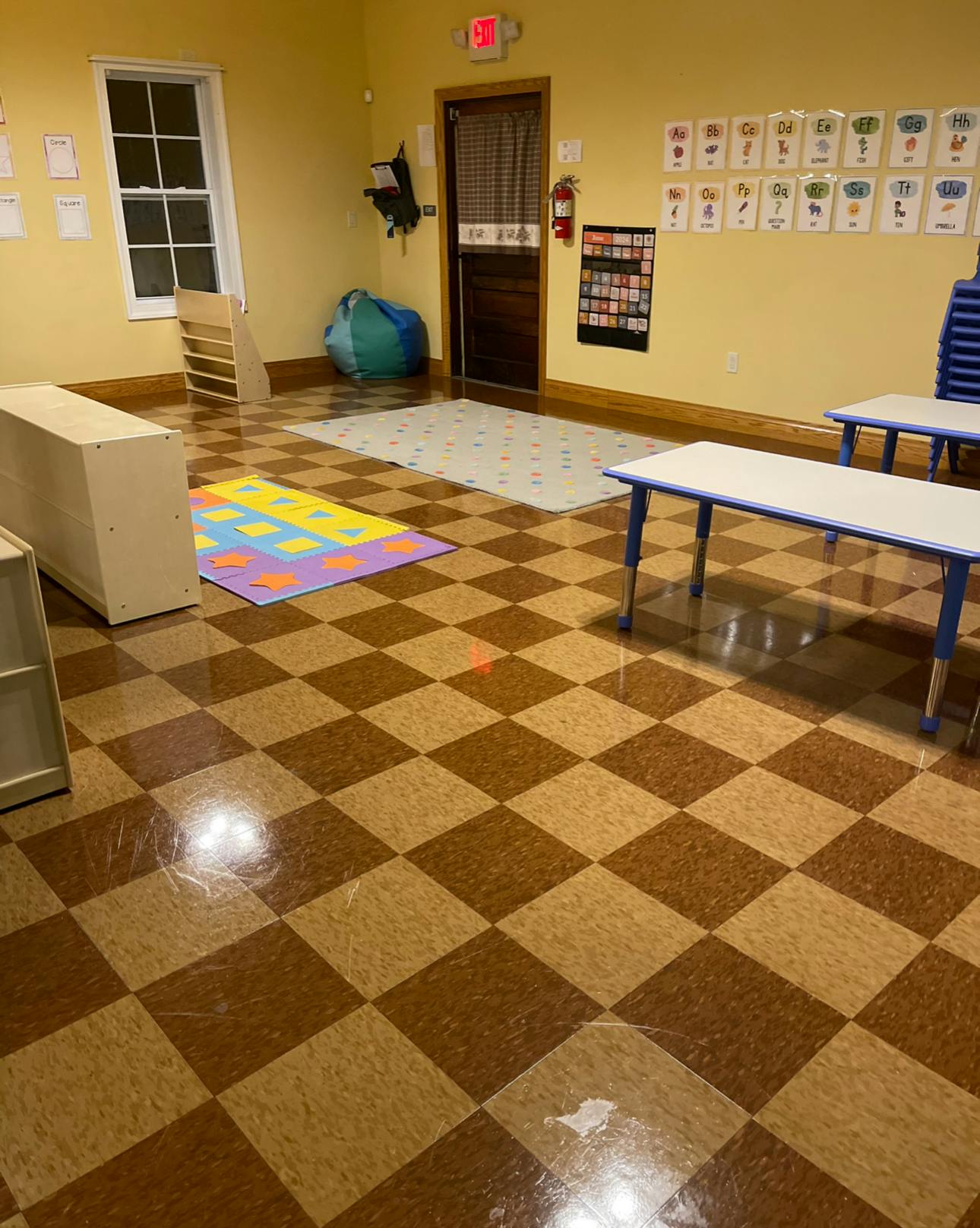 Empty classroom with checkered floor, tables, and colorful playmat
