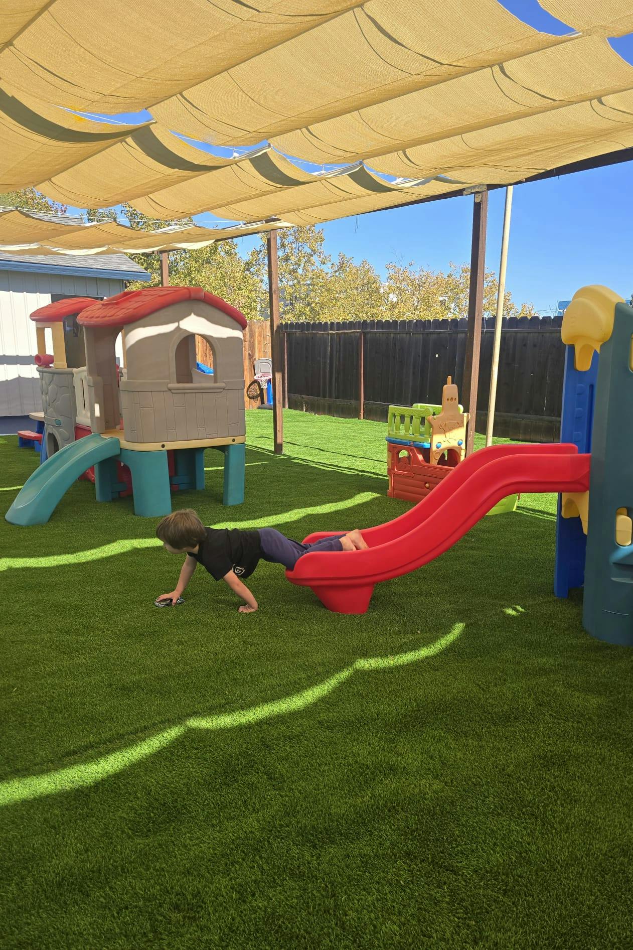 Child crawling out of a small plastic slide on an artificial grass playground