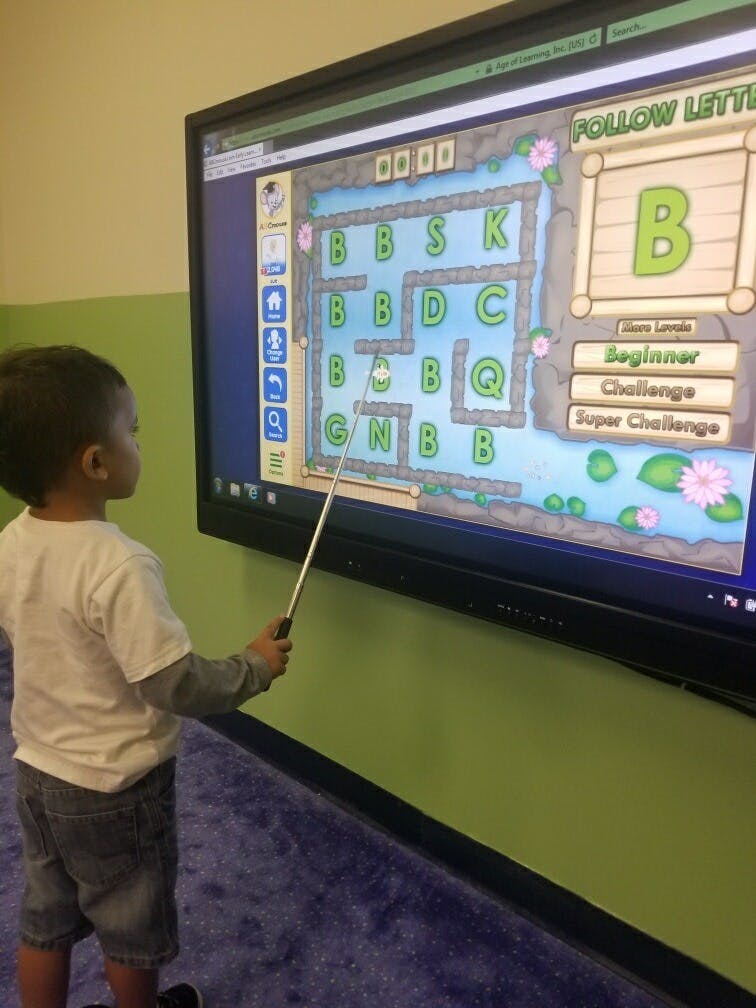Child using a pointer on a large screen displaying a letter maze game