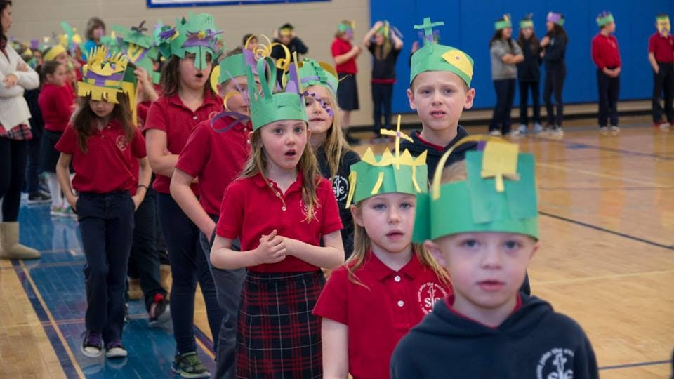 Children in red shirts and paper crowns walking in a line