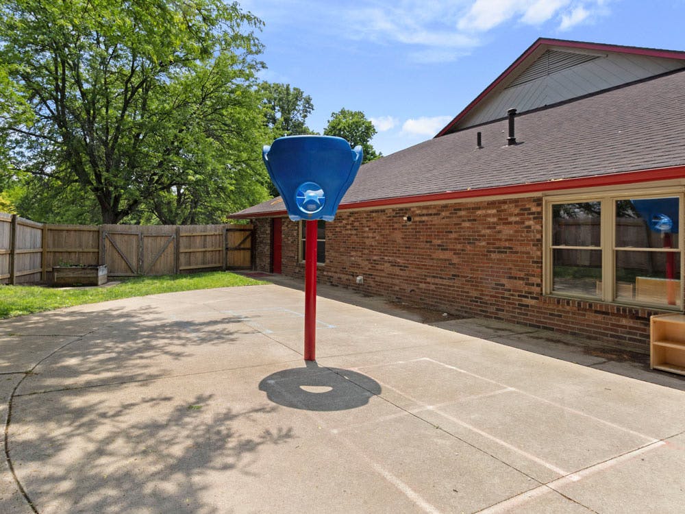 Basketball hoop on a concrete court next to a brick building with a wooden fence