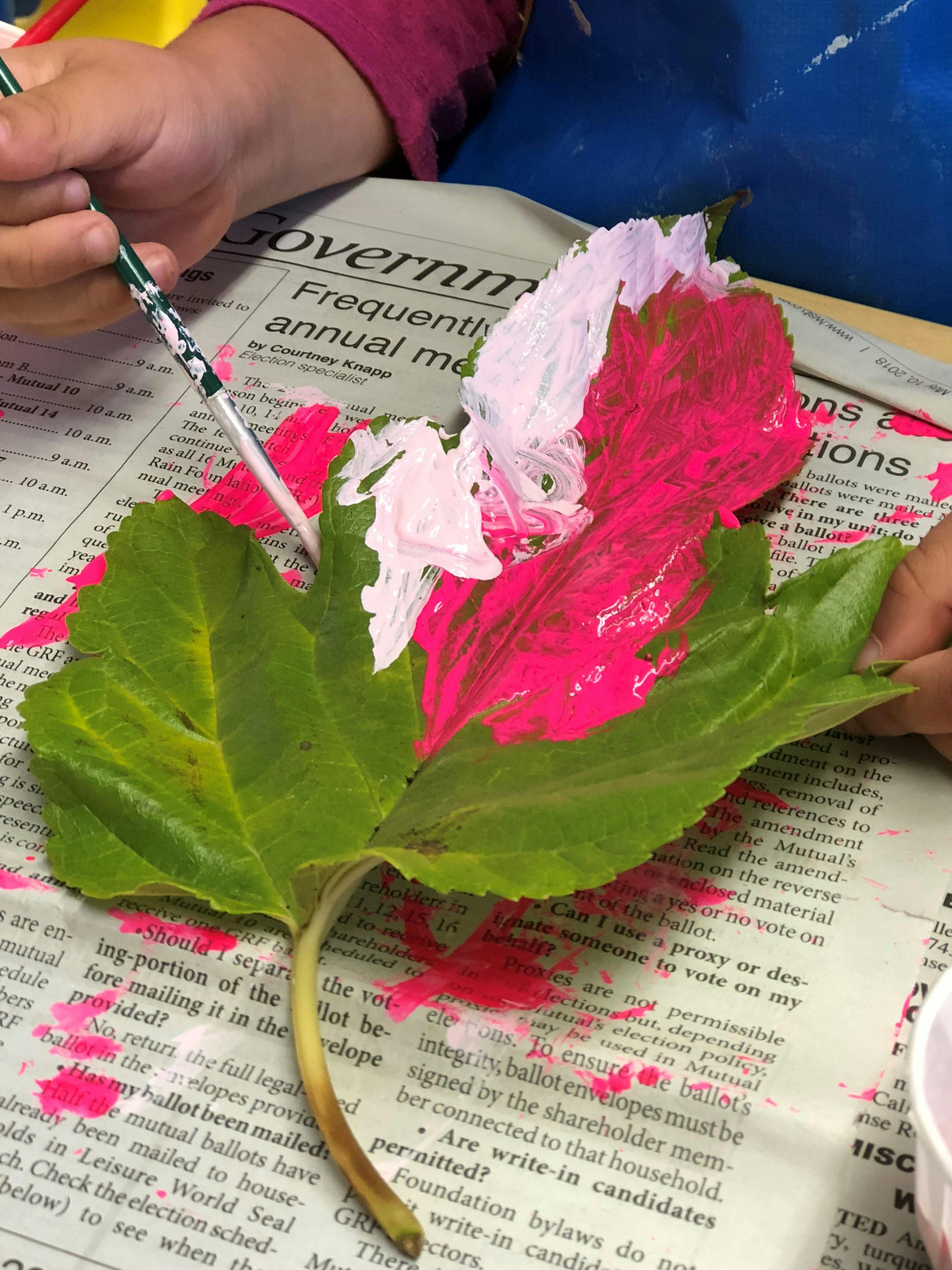 Child painting a green leaf with pink and white paint