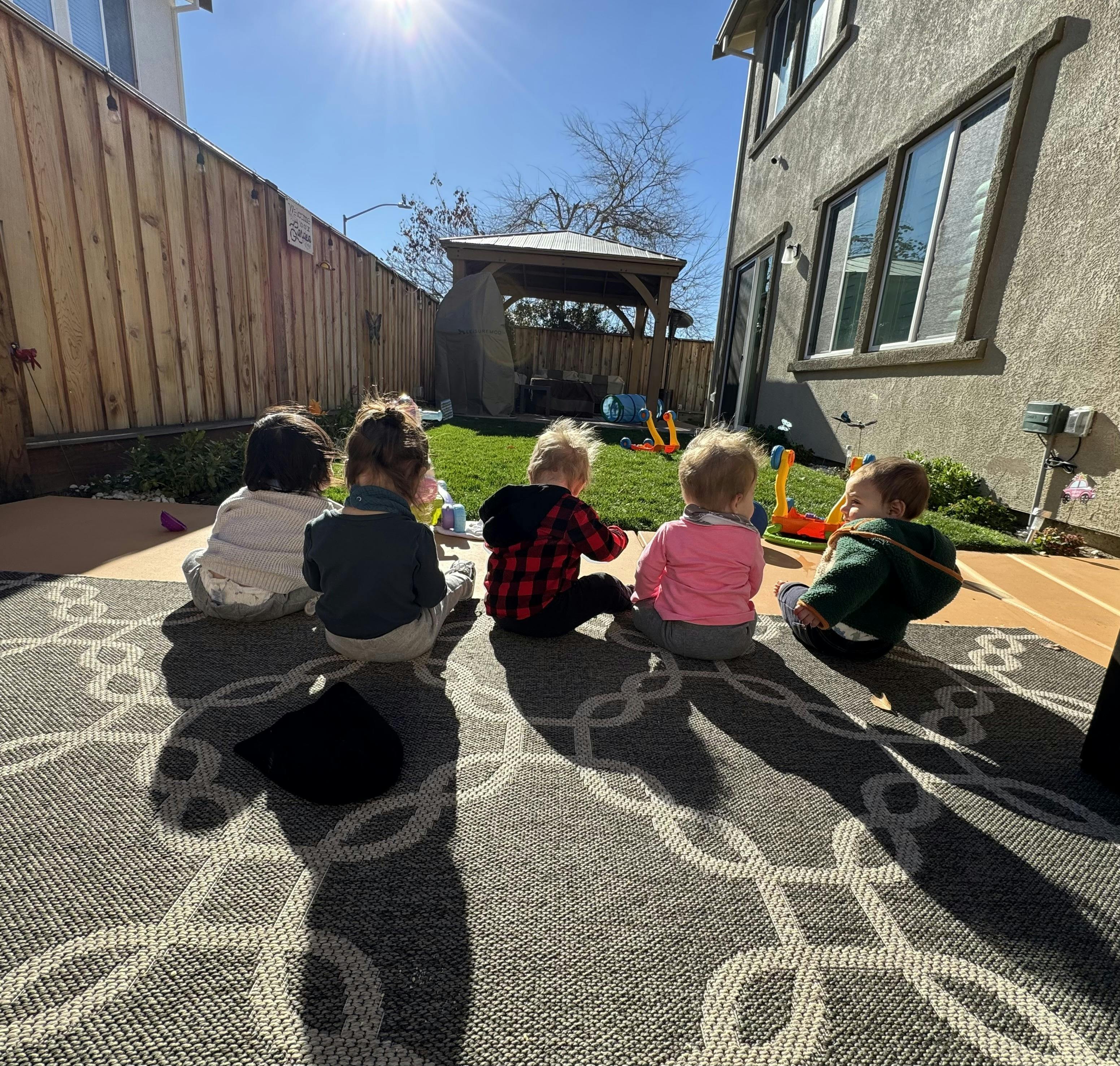 Five children sitting on a patio rug with their backs to the camera
