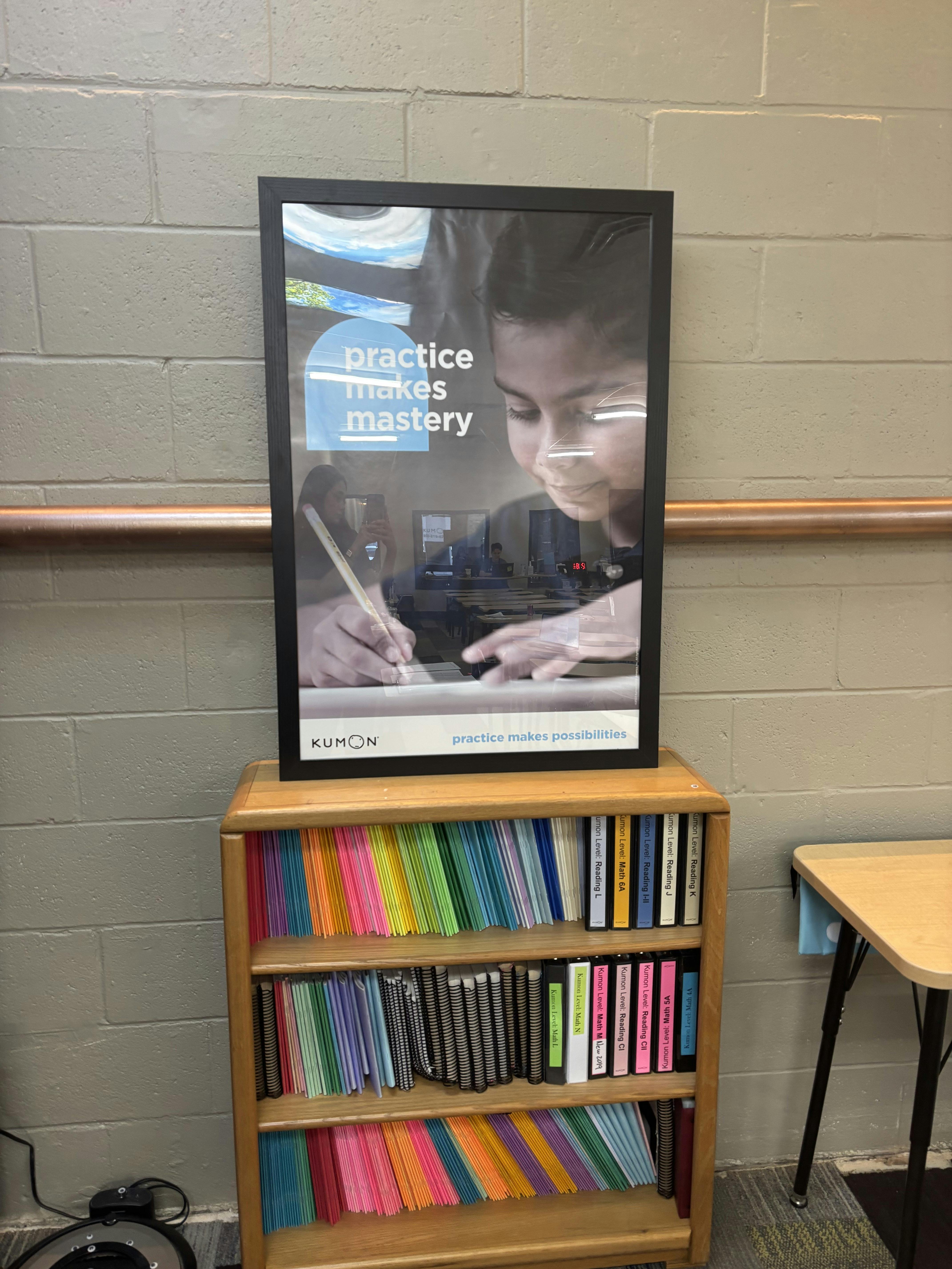 Kumon poster with 'practice makes mastery' over an image of a child writing