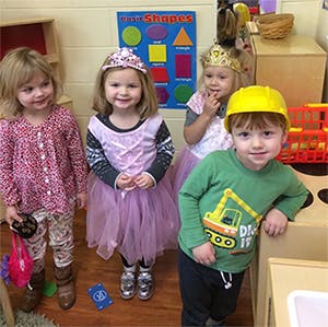 Four children in a classroom, one wearing a hard hat
