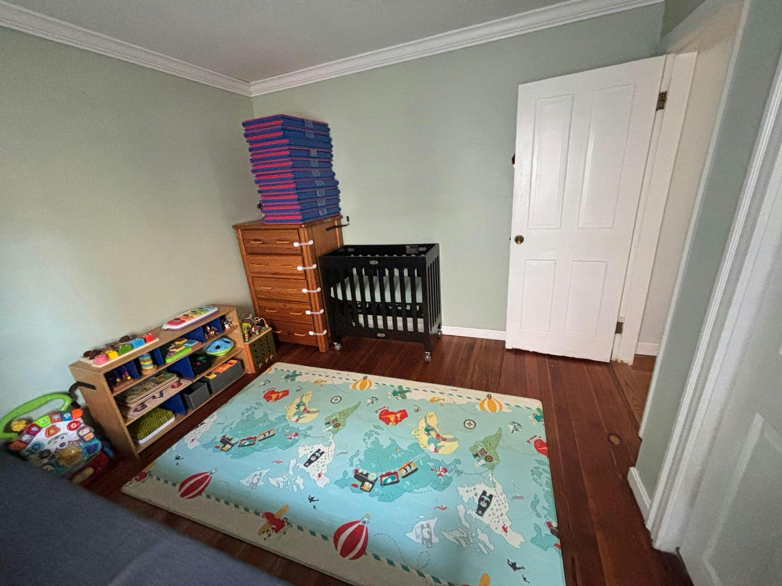 Childs bedroom with a crib, storage shelves, and a world map floor mat