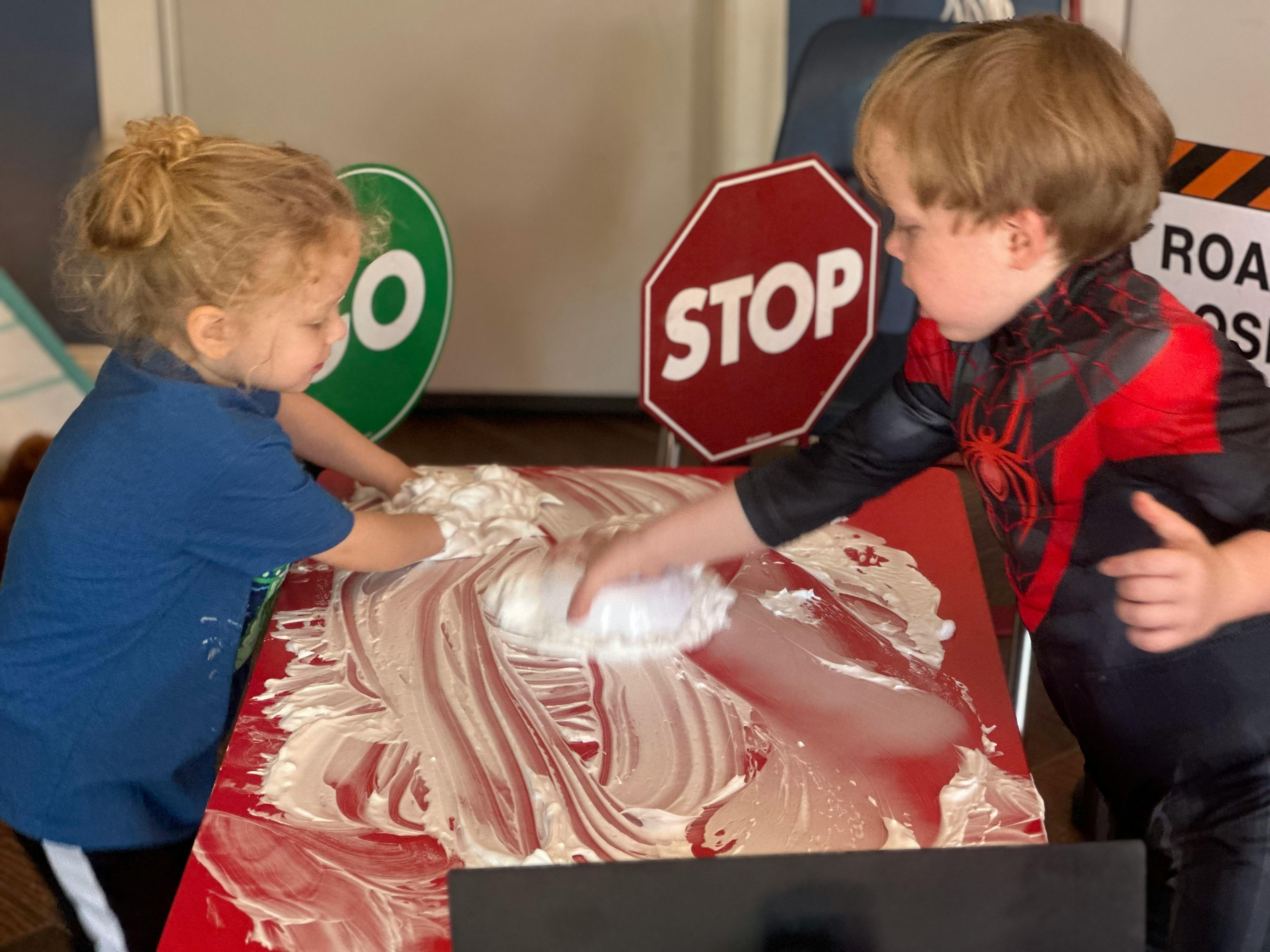Two children playing with shaving cream on a red surface