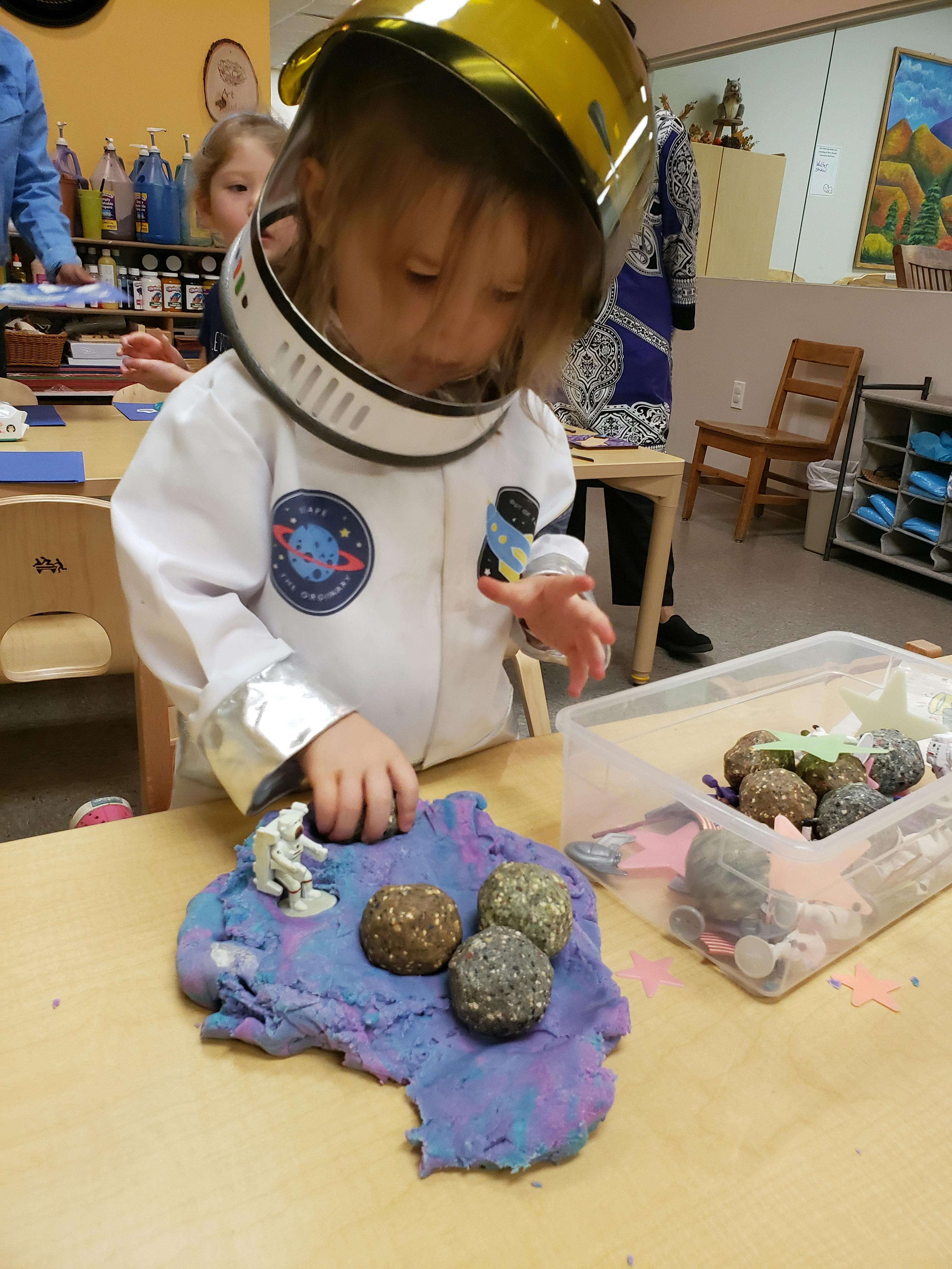 Child in astronaut costume playing with modeling clay and small objects