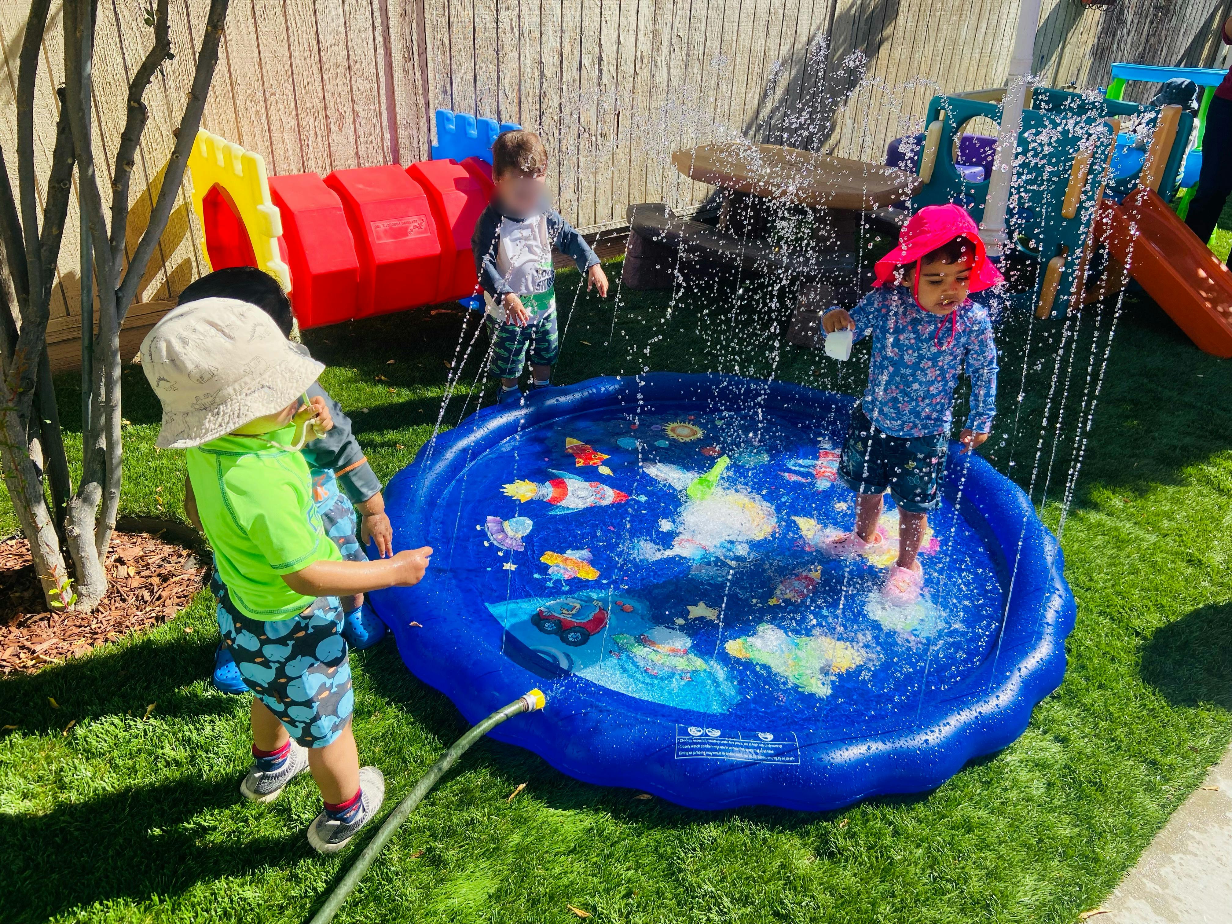 Children playing in a blue inflatable splash pad with water spraying