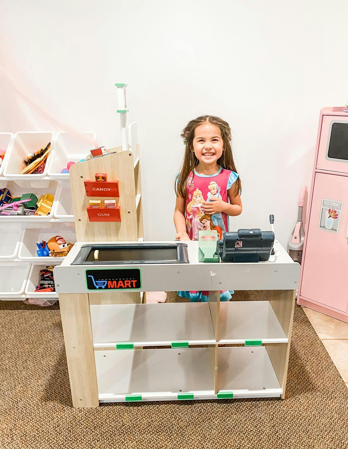 Child standing behind a toy checkout counter with "MART" visible