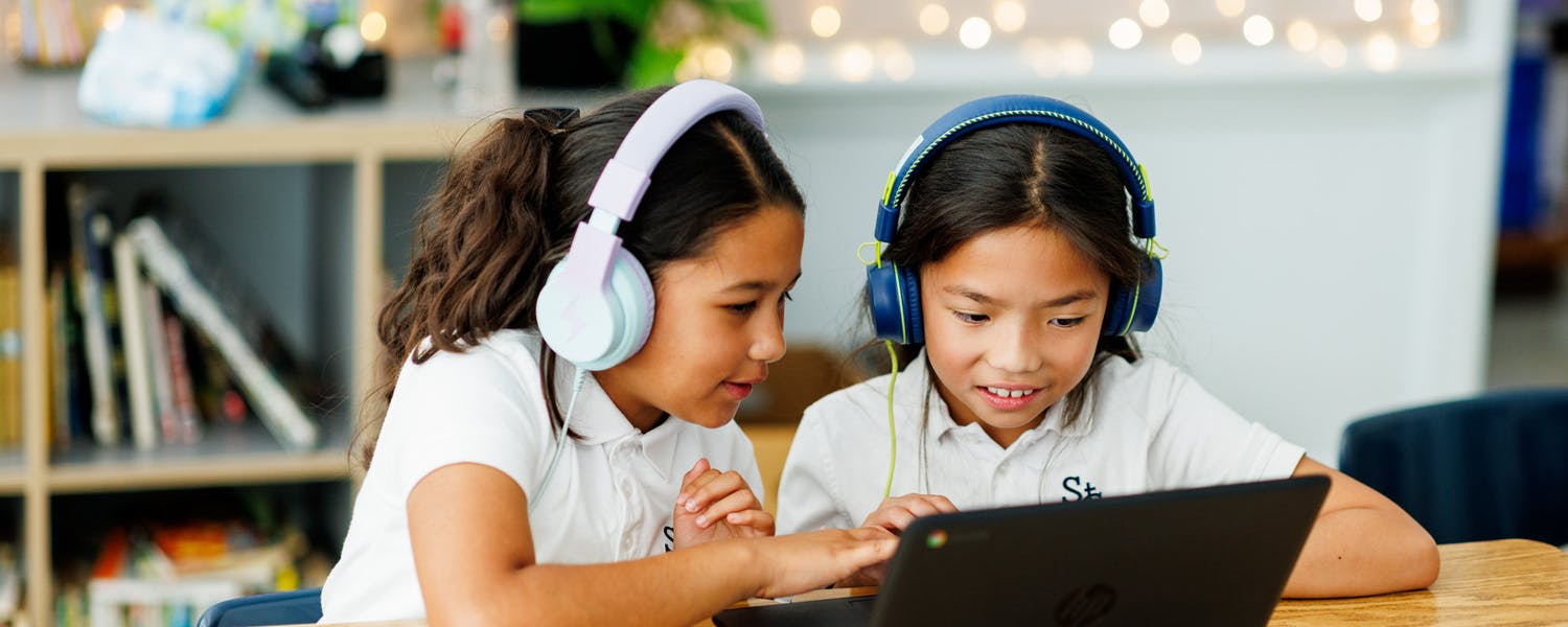 Two children with headphones using a laptop in a classroom