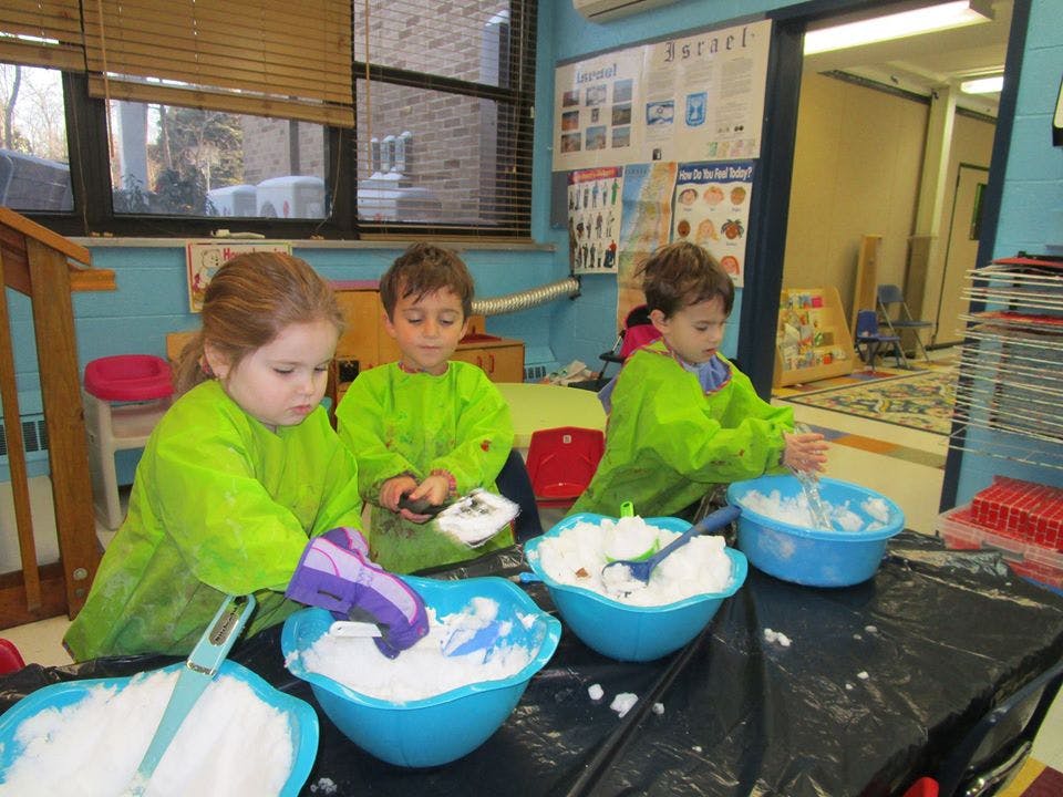 Three children in green smocks playing with white material in blue bowls