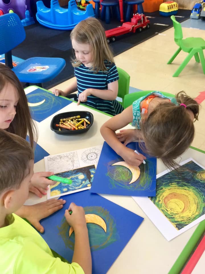 Children coloring crescent moon shapes on blue paper