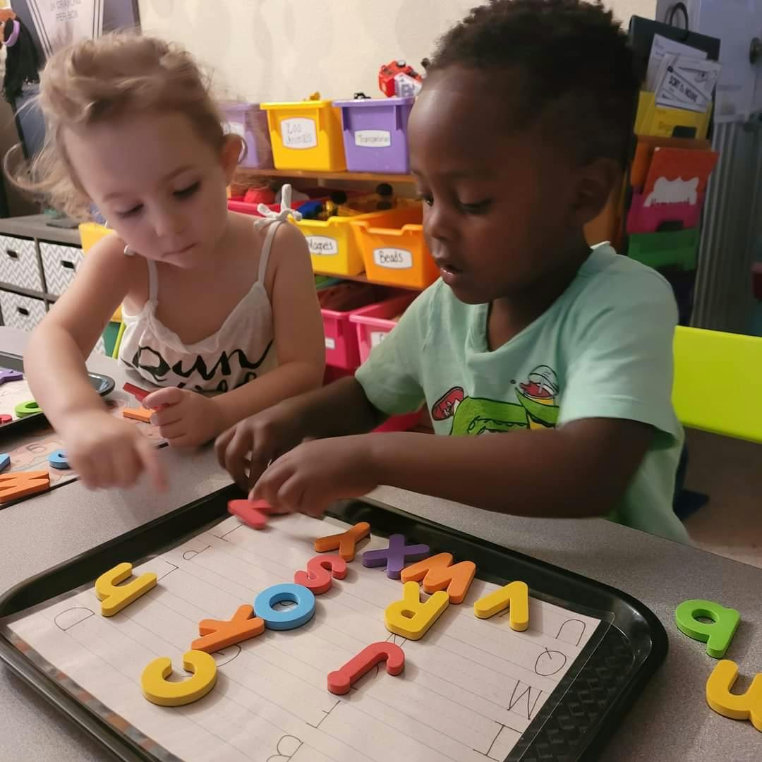 Two children playing with alphabet letters on a tray