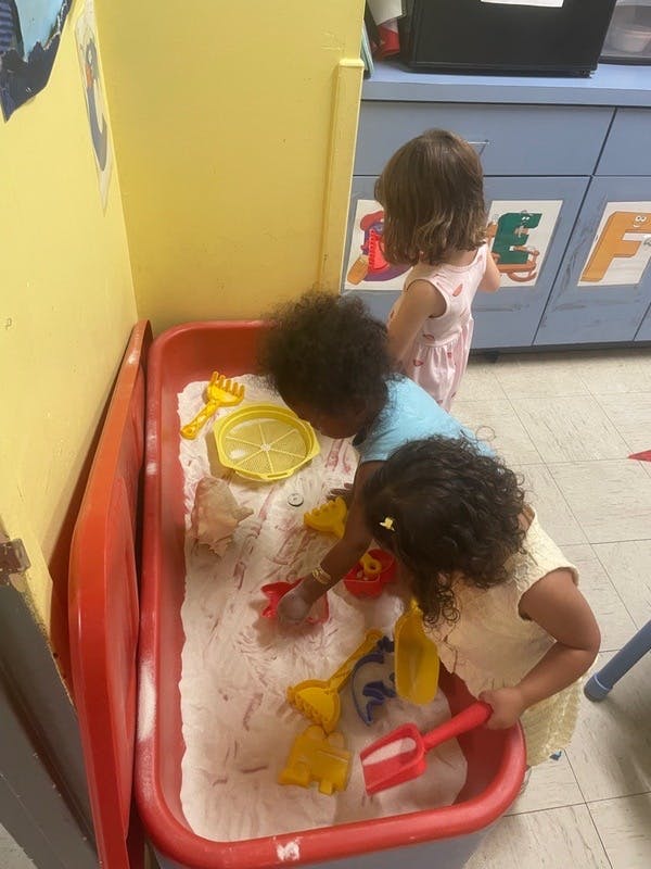 Three children playing in a sandbox with various toys