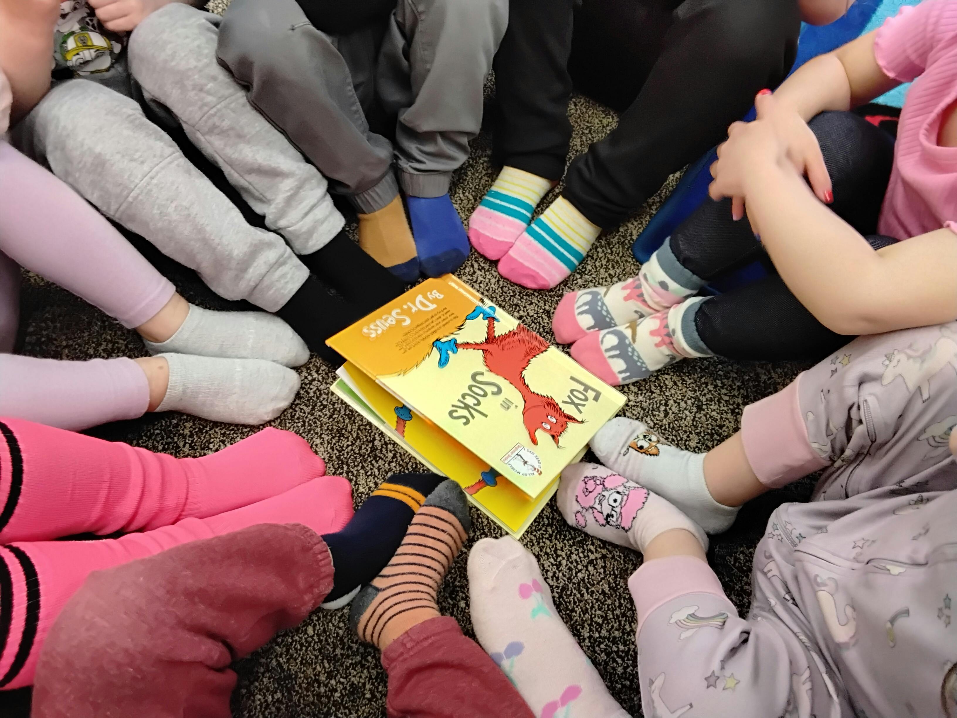 Children sitting in a circle around a book titled book "Fox in Socks"