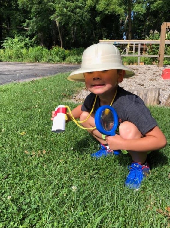 Child in a hat crouching in grass with a magnifying glass and bug viewer