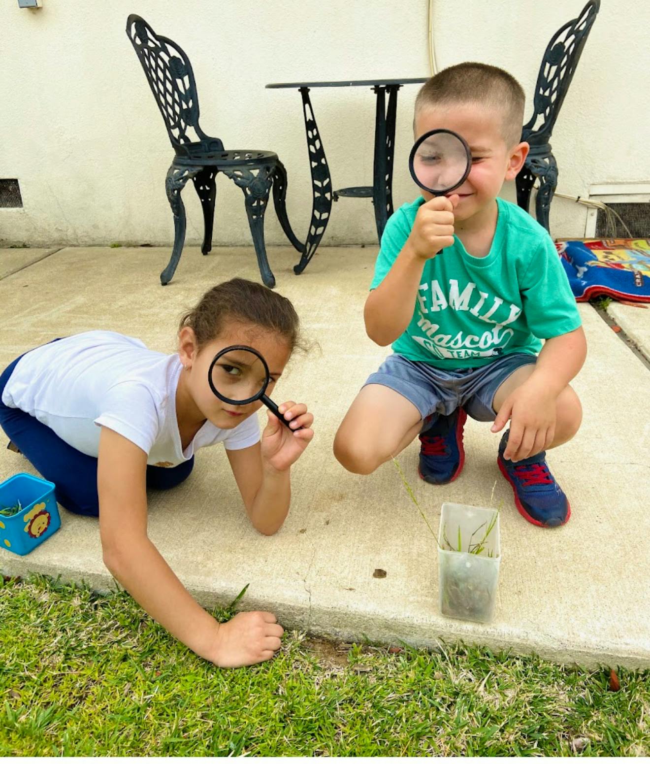 Two children crouching on a patio and looking through magnifying glasses