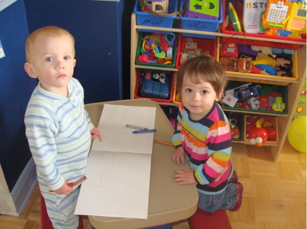 Two children standing at a table with an open notebook and blank notebook