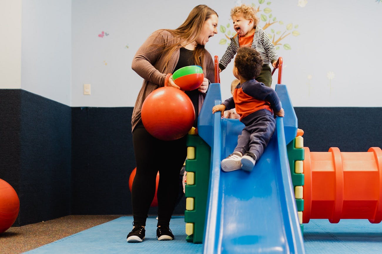 Adult and two children playing on a slide and with balls in a play area