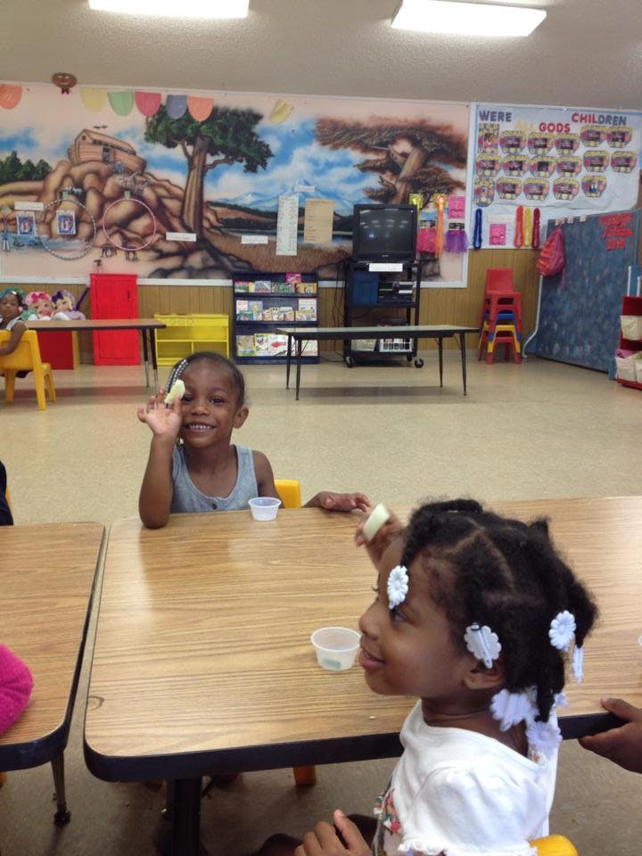 Child holding up food at a table in a classroom