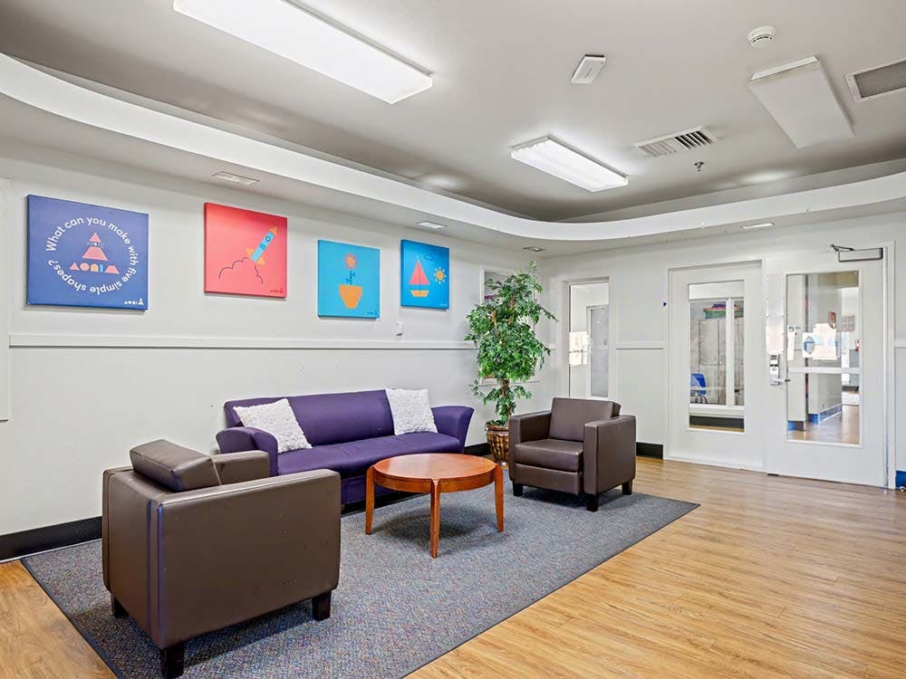 Lounge area with a purple sofa, two brown armchairs, and a round wooden coffee table
