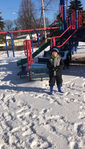 Child standing in snow in front of a playground structure