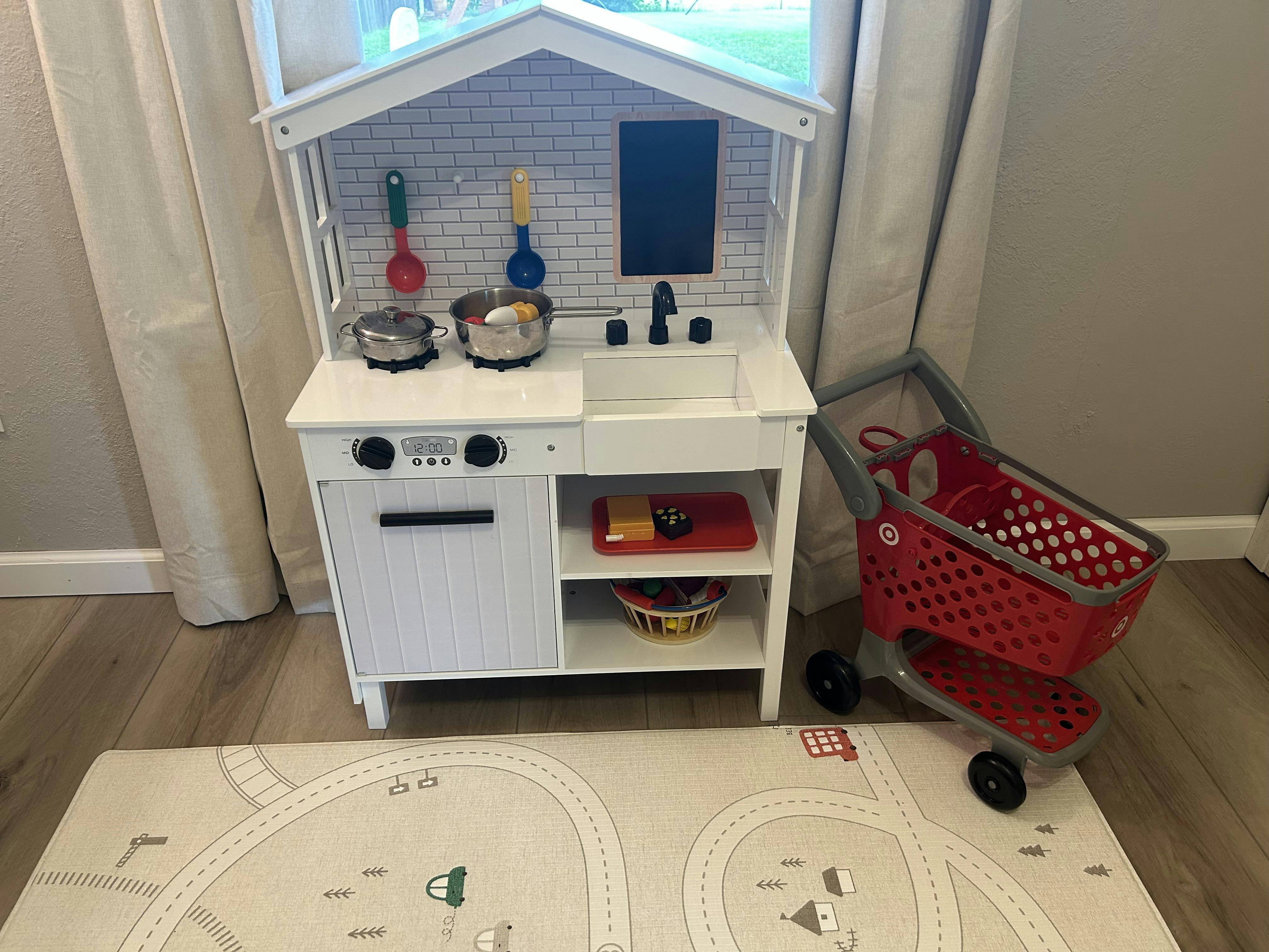 White play kitchen with a red toy shopping cart next to it