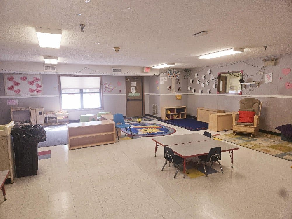 Empty classroom with small tables and chairs, play kitchen, and storage shelves