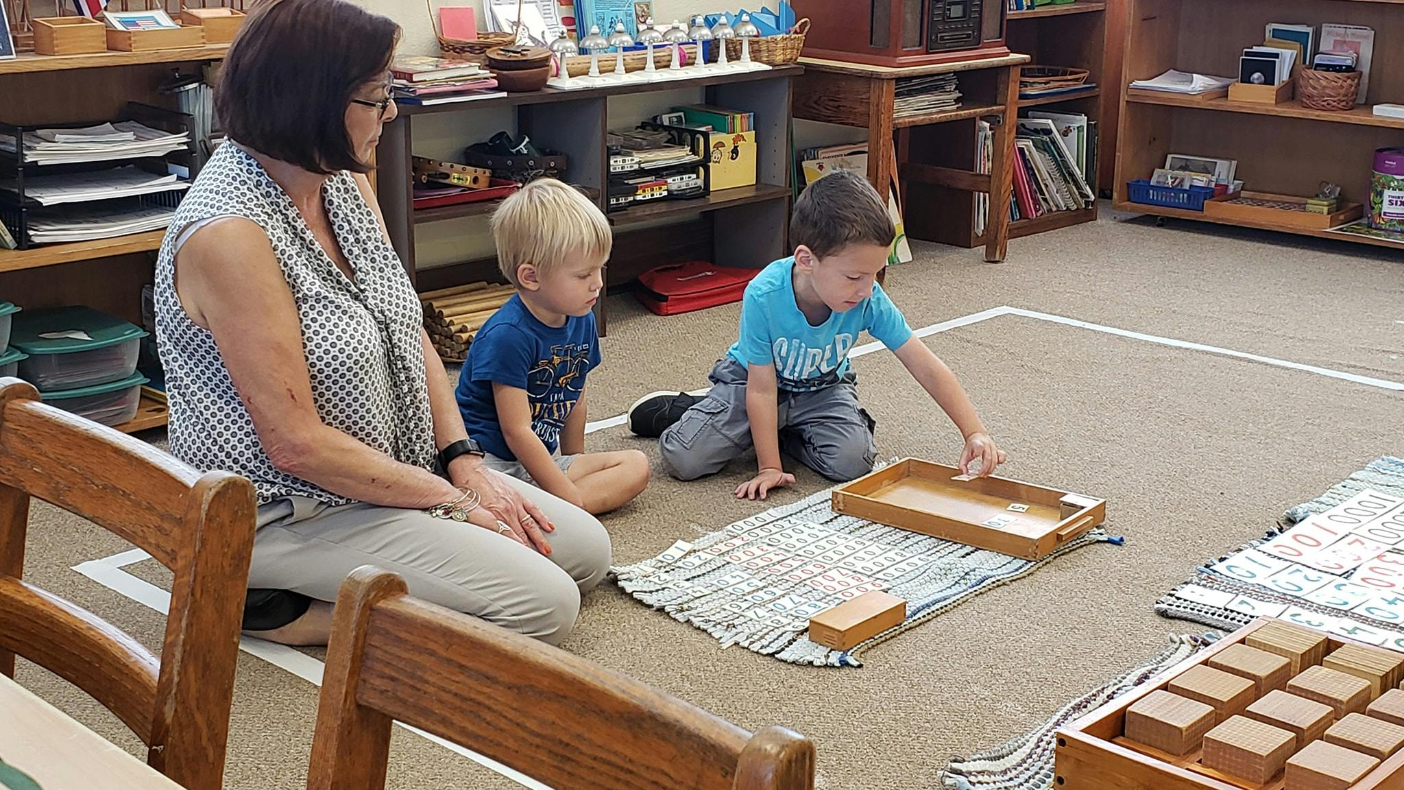 Adult and two children on floor, one child playing with wooden blocks