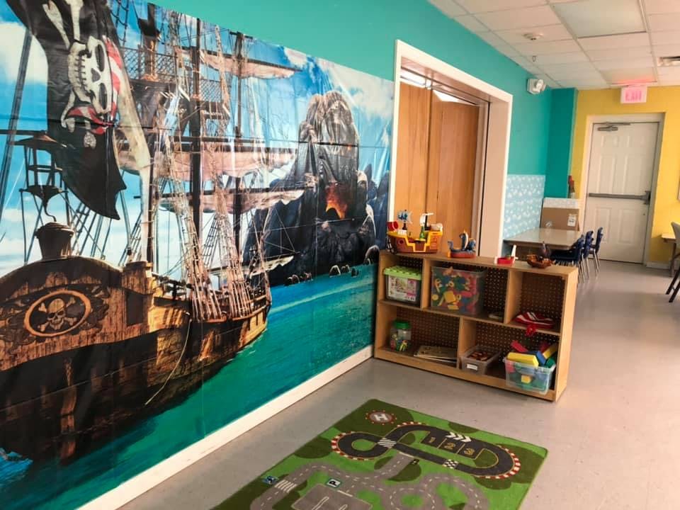 Wall mural of a pirate ship on water next to a bookshelf with toys