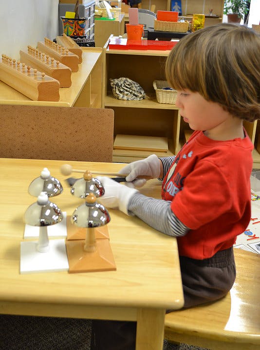 Child wearing gloves playing with bells on a table