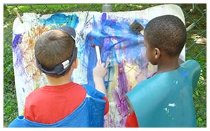 Two children painting on a canvas outdoors easel