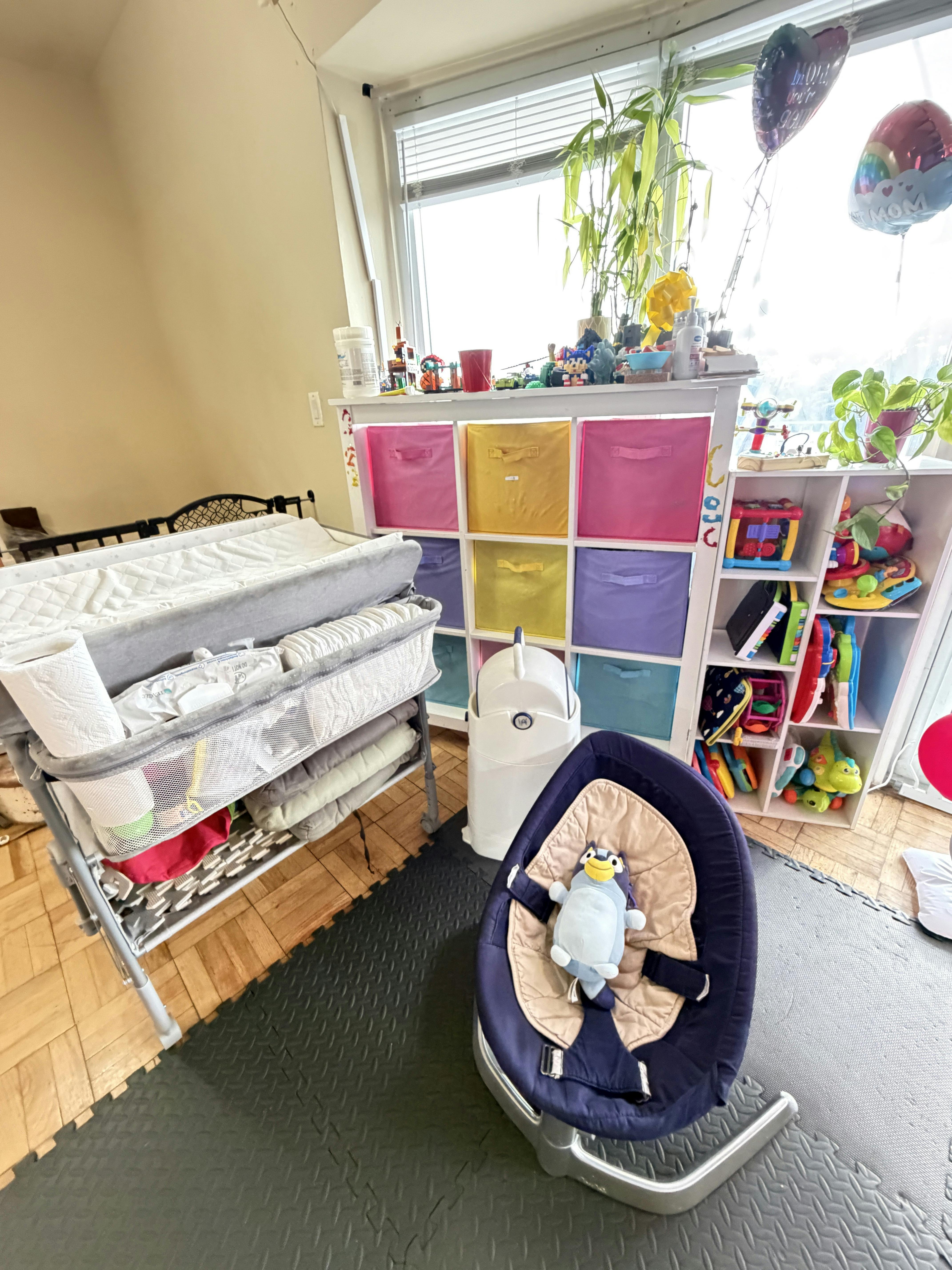 Baby swing with a plush toy in a room with a changing table and toy storage