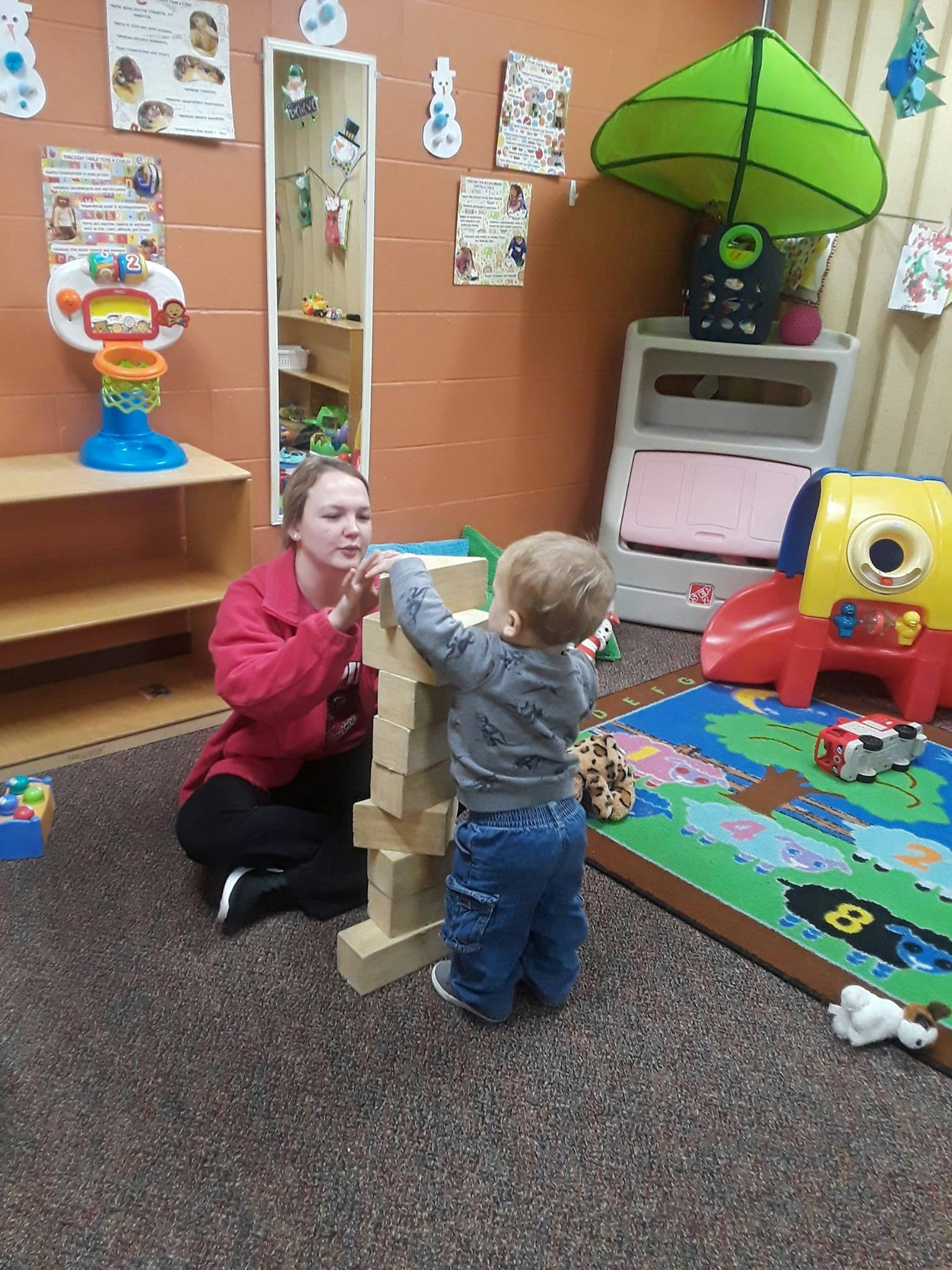 Person and child building a tower with wooden blocks in a play area
